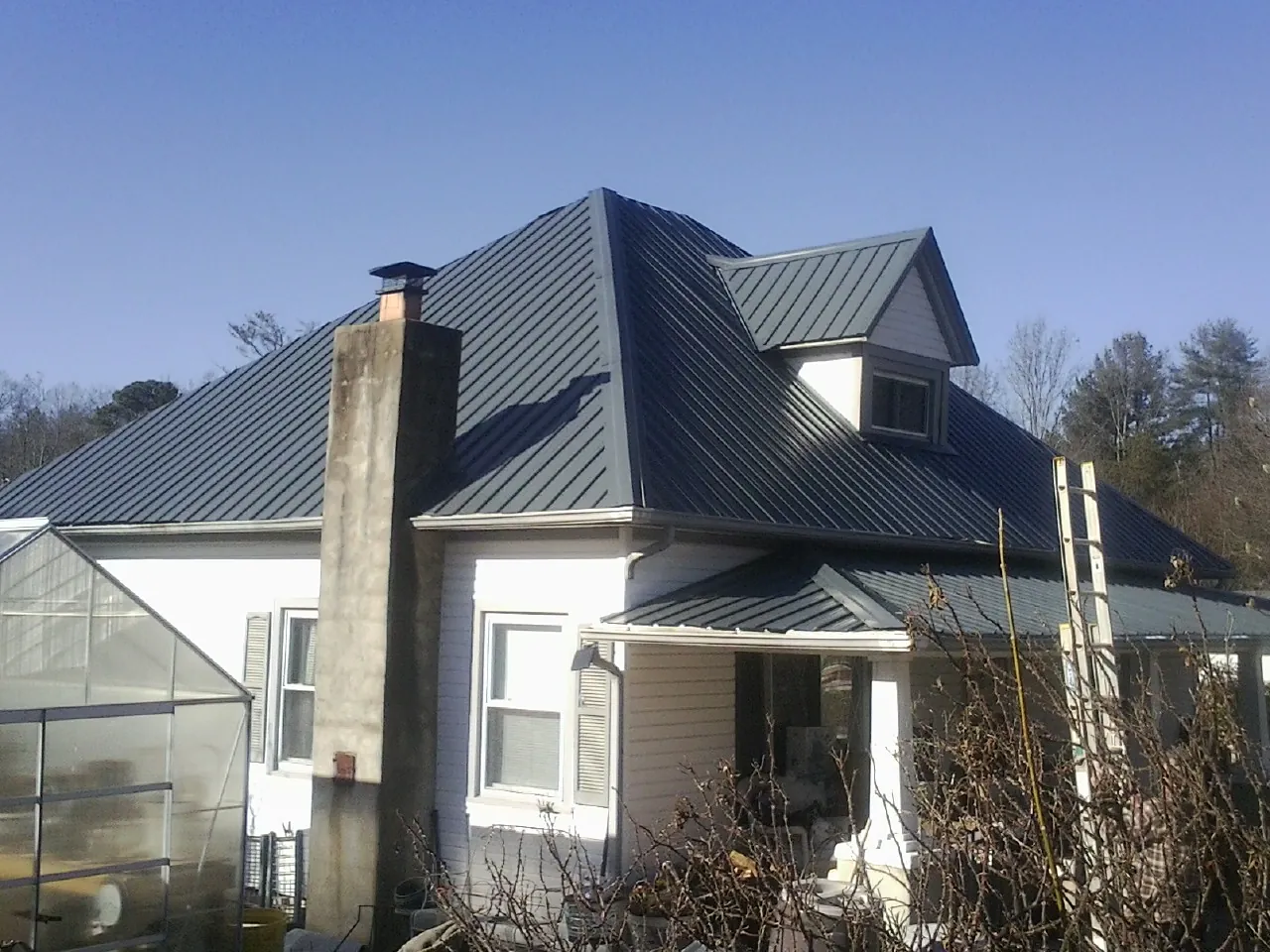 Dark blue standing seam metal roof on a white farmhouse with dormer — Slate & Tile Roof Repair by Roofing Brothers in Vicksburg
