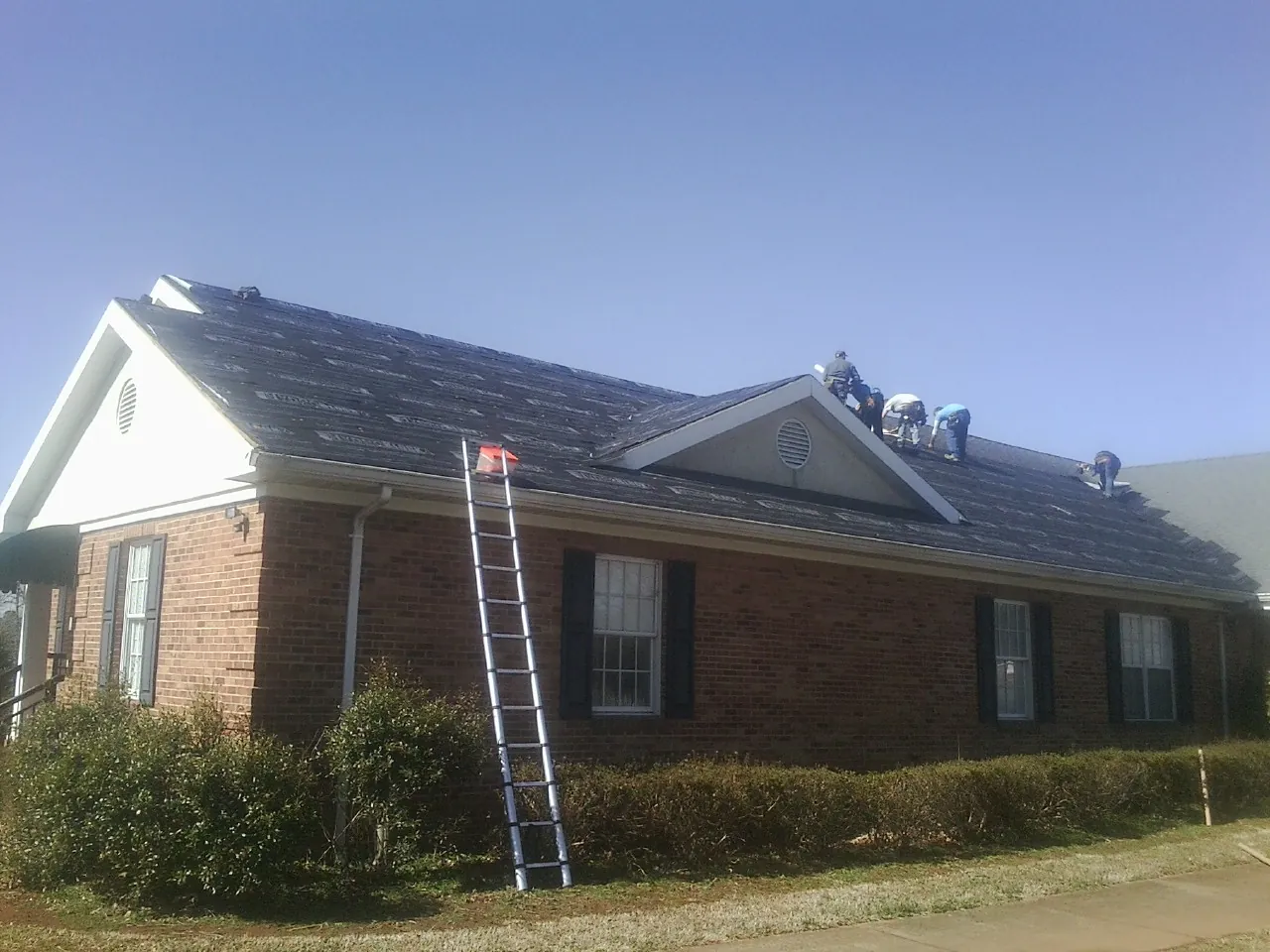 Crew tearing shingles off a brick ranch roof with a ladder set — Emergency Roof Repair work by our crew in Vicksburg