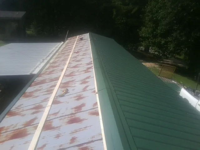 Old rusted panels beside newly installed green metal roofing — Wind Damage Roof Repair by Roofing Brothers in Vicksburg
